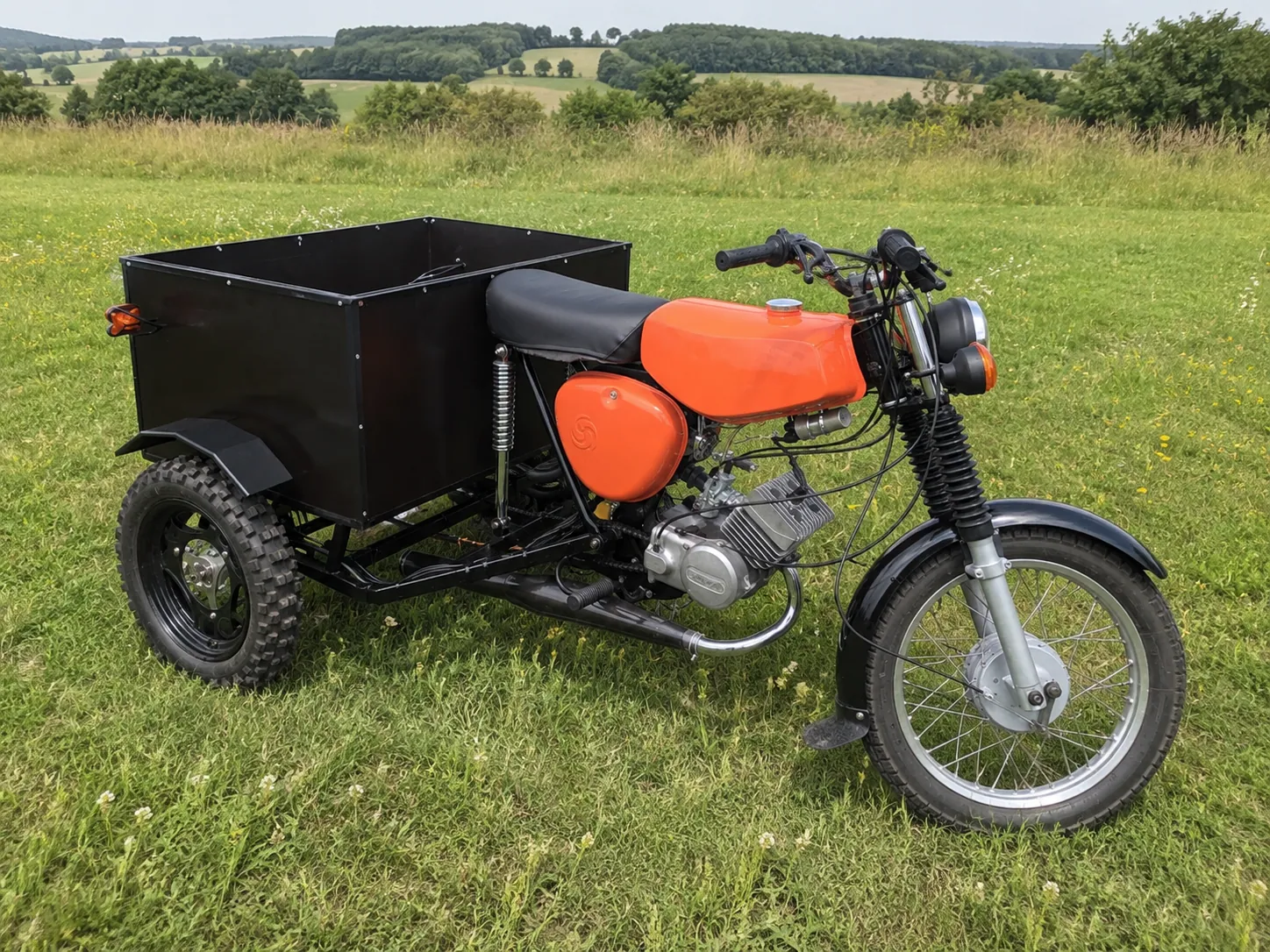 Orangefarbene Simson als dreirädriger Lasten-Prototyp mit schwarzem Transportkasten auf einer Wiese
